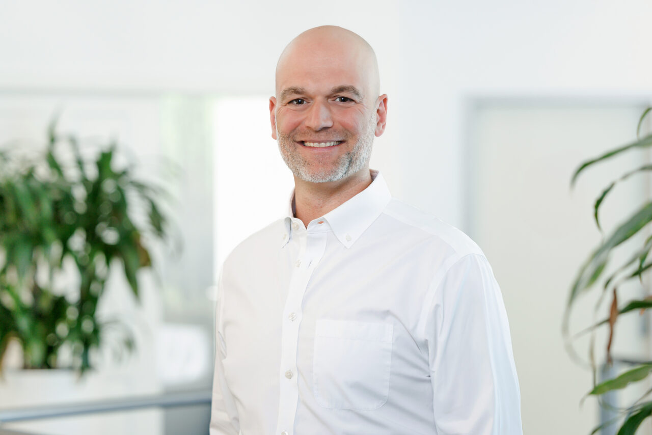 Zu sehen ist Steuerberater und Geschäftsführer der DHW, Christian Deák in einem weißen Hemd.
